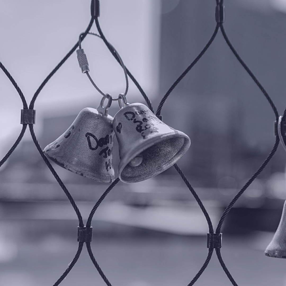 Bells tied to a chainlink fence in a purple hue