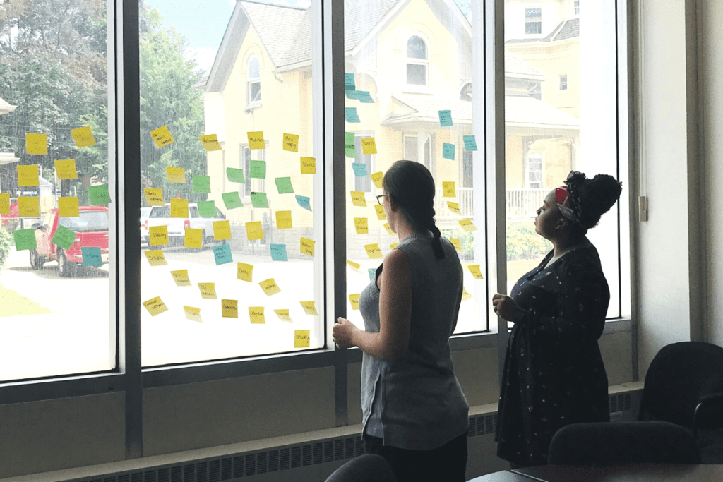 image of two women looking at post it notes on a window, reviewing creative ideas and innovative solutions for issues like homelessness